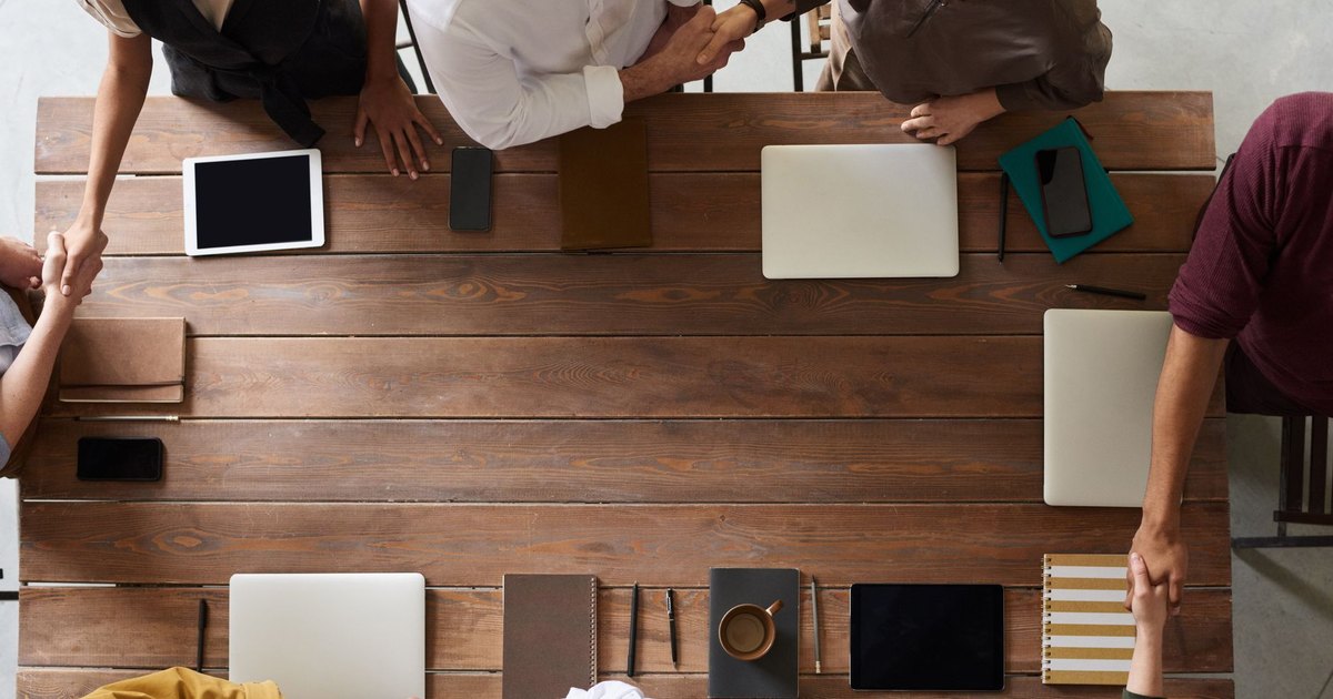 Group of adults having a business meeting, discussing plans around a wooden table with tech devices.