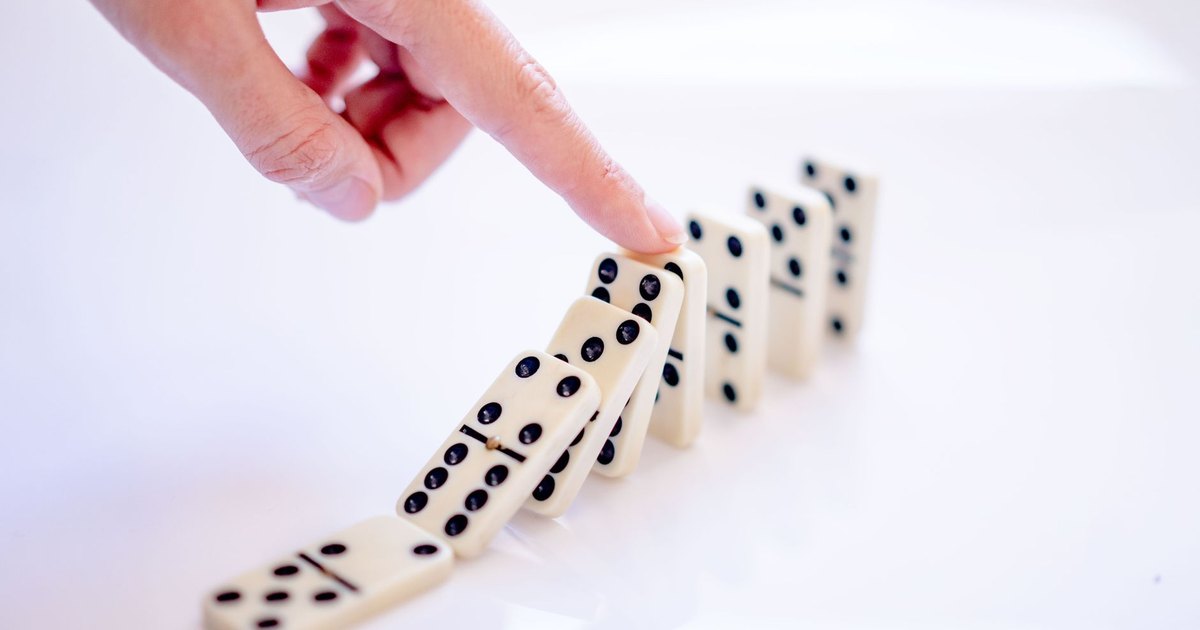 A close-up shot of a hand pushing dominoes, illustrating cause and effect.