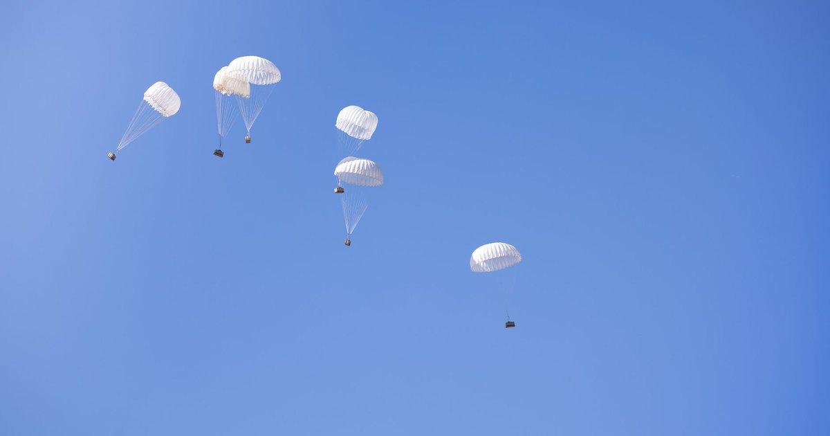 Multiple parachutes drop cargo boxes in a clear blue sky, showcasing aerial delivery technology.