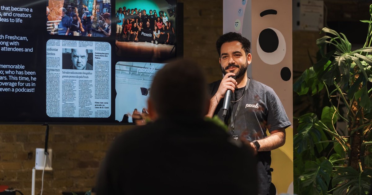 A speaker holding a microphone addresses an audience indoors at a presentation event.