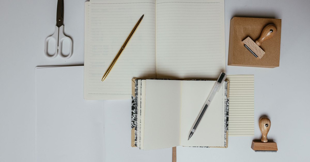 Flat lay of stationery including notebooks, pens, scissors, and stamps on a desk. Ideal for office or school themes.