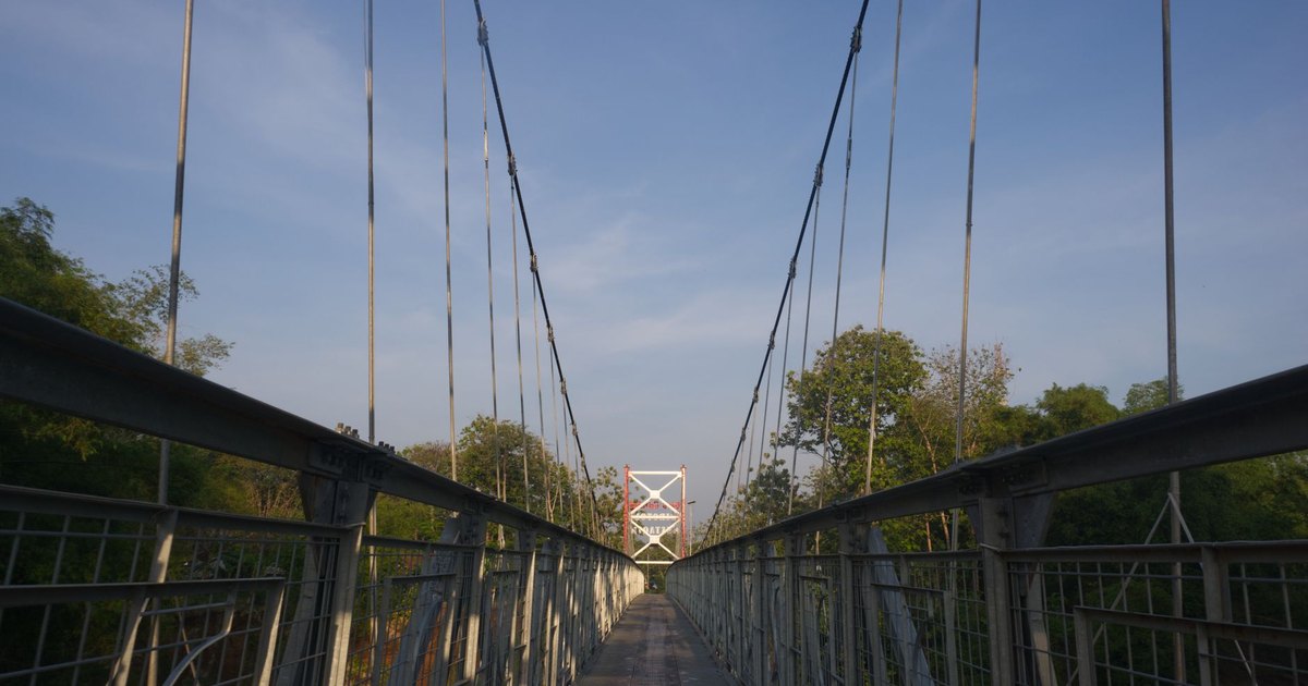 Suspension bridge stretching over greenery against a clear blue sky, captured in daylight.