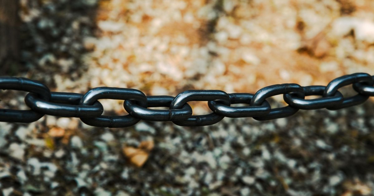 Detailed view of a sturdy black metal chain outdoors on a blurred background.
