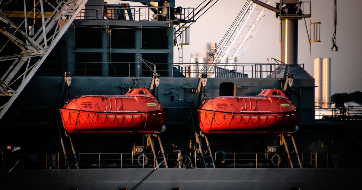 Close-up of a ship displaying two vibrant orange lifeboats attached to its side.