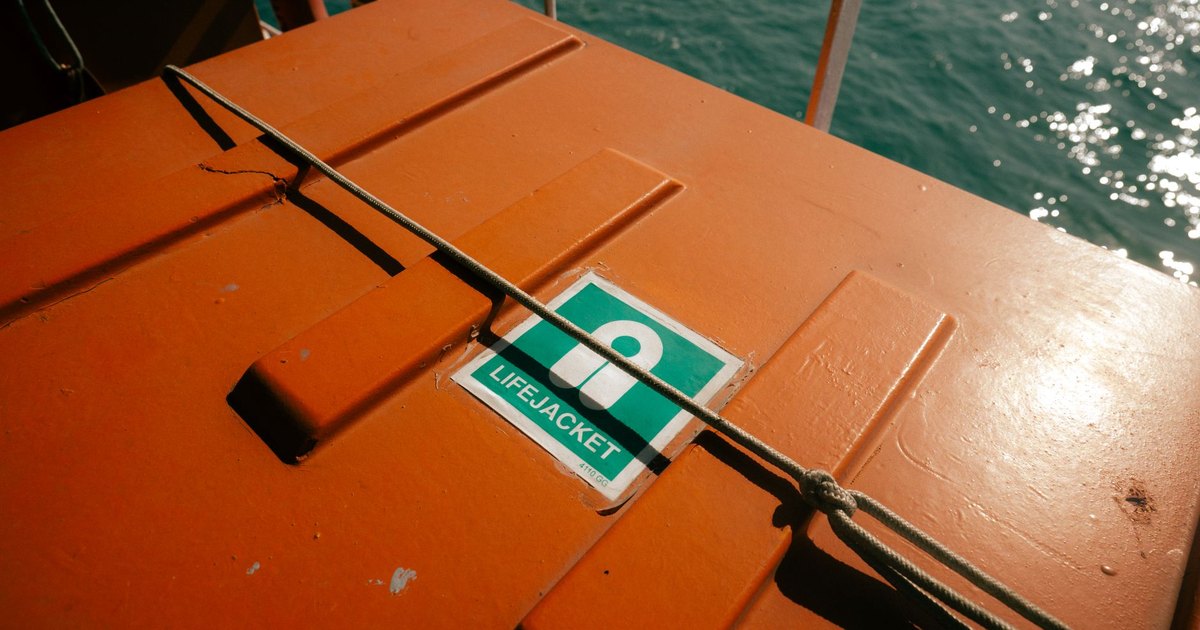 Orange lifeboat storage with lifejacket sign on a clear sunny day at sea.