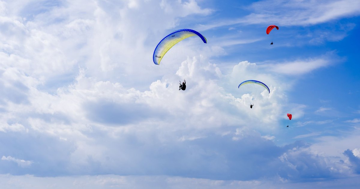 Colorful paragliders soar over the ocean against a backdrop of blue sky and clouds, capturing the thrill of aerial adventure.