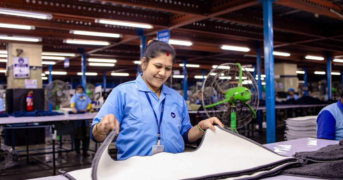 A woman in a blue uniform folding textiles in a brightly lit factory.