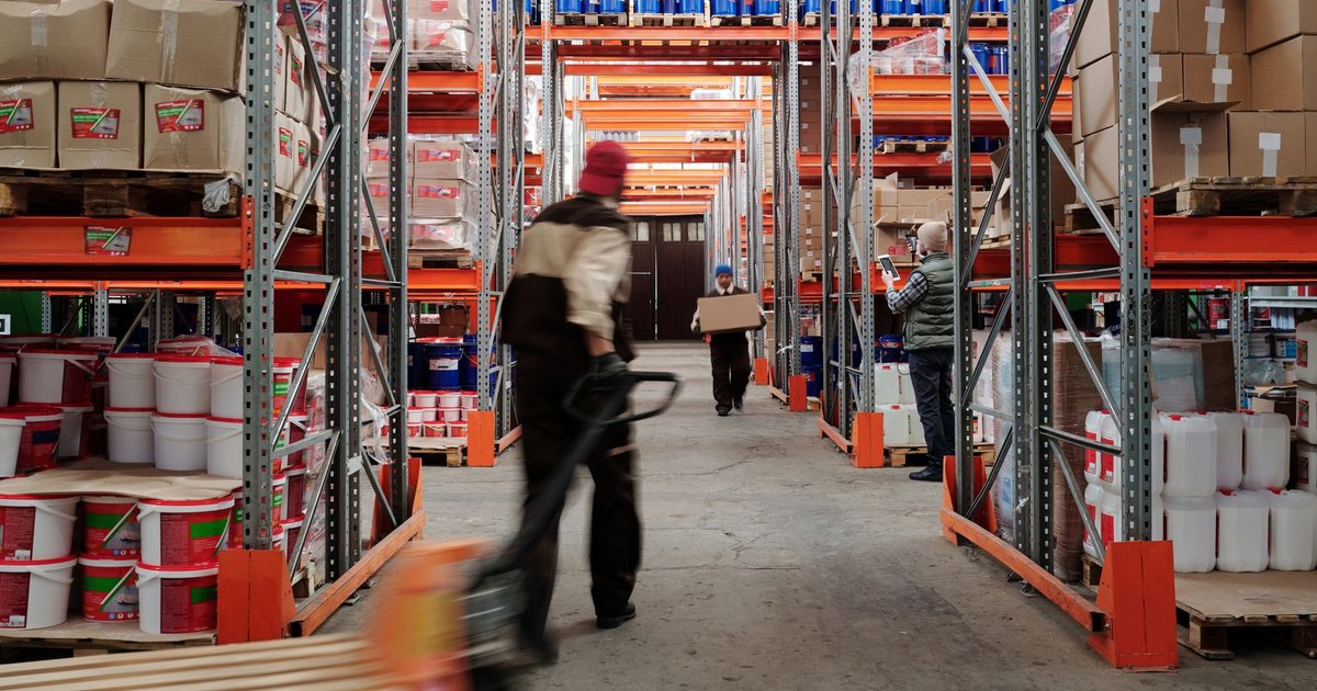 Warehouse interior with workers organizing shelves full of boxes and containers.