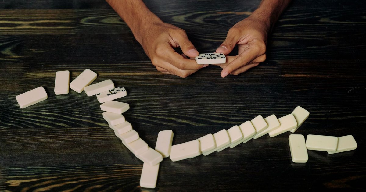 High-angle view of hands holding and arranging dominoes on a wooden table symbolizing strategy and impact.