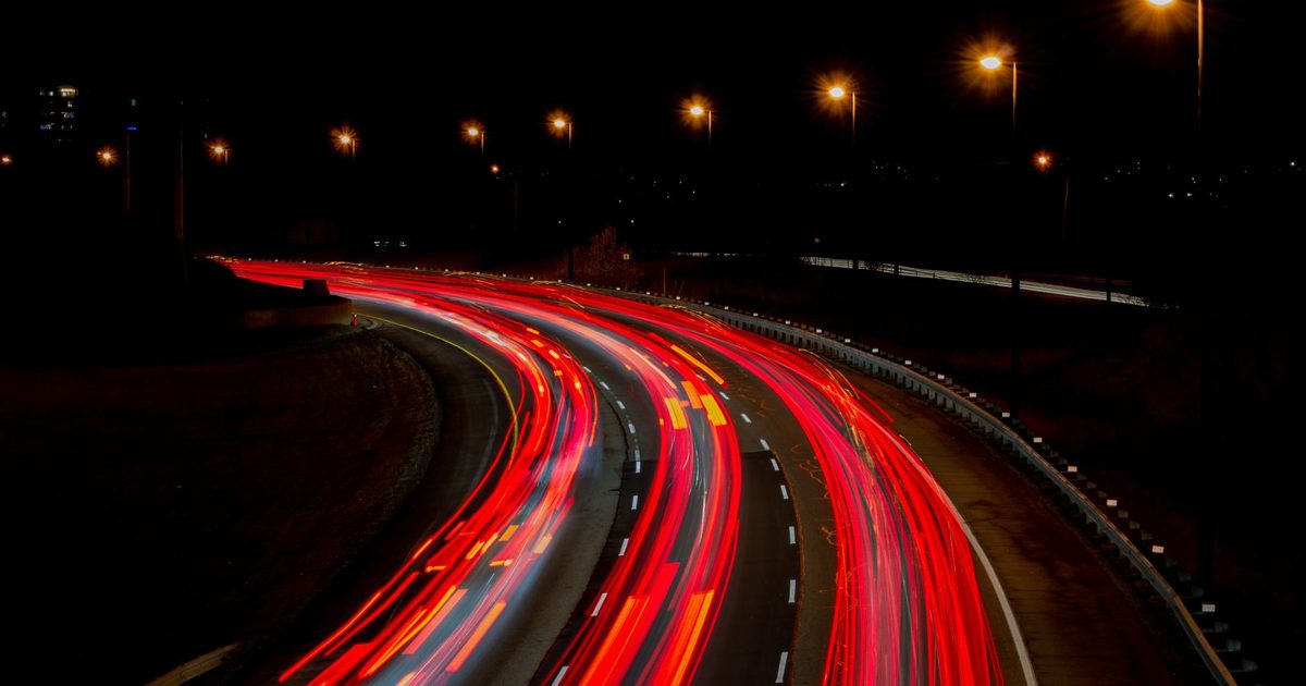 A captivating long exposure of a highway at night, showcasing vibrant light trails under streetlamps.