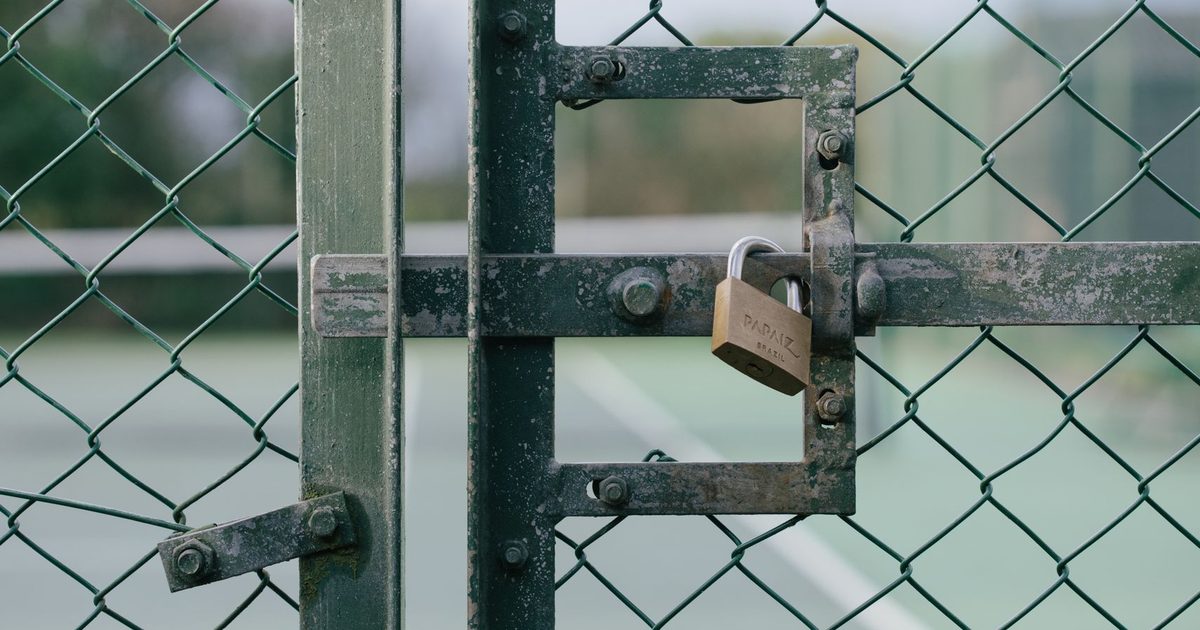 Close-up of a locked gate with chain link fence at a tennis court outdoors.